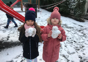 Dzieci stoją ze śnieżkami podczas pobytu na przedszkolnym placu zabaw.